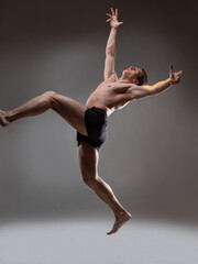 Fototapeta premium Muscular man in an artistic pose, portrait on a gray background. The guy is an athlete in a jump or fall. Expressive pose
