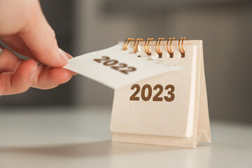 a woman's hand turns over a calendar sheet. year change from 2022 to 2023 - obrazy, fototapety, plakaty