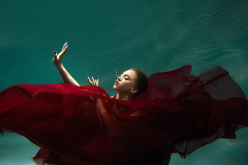 Beautiful underwater shooting, a young woman in a red dress with a long skirt swimming underwater,...