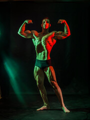 Handsome bodybuilder doing classic double biceps pose, looking away, on dark background