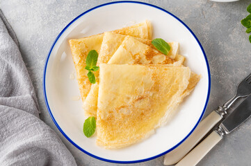 Stack of traditional thin pancakes or crepes on a plate with honey and sour cream on a gray concrete background. Food for Maslenitsa. Copy space