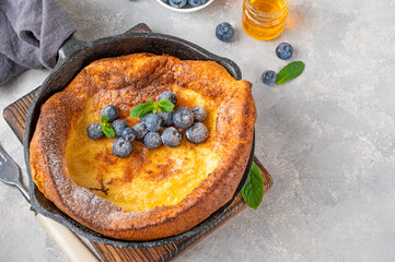 Homemade Dutch Baby pancake with fresh blueberries, mint and sprinkled with icing sugar in iron...