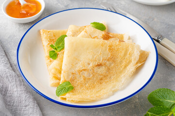 Stack of traditional thin pancakes or crepes on a plate with honey and sour cream on a gray concrete background. Food for Maslenitsa. Copy space