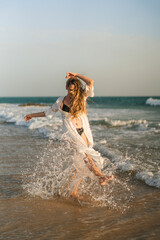 Chica joven con pelo largo en bikini en la orilla de la playa jugando con el agua del mar