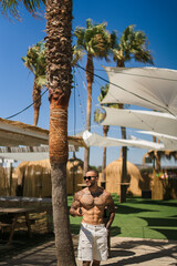 Chico joven musculoso tatuado  tomando el sol y haciendose fotos en pub en la playa