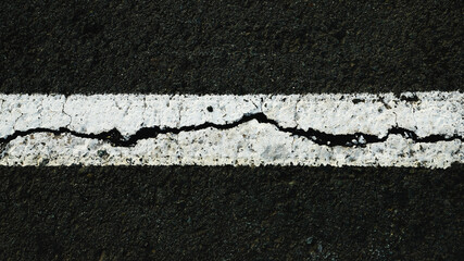 Fototapeta premium Worn white road line on cracked asphalt close-up