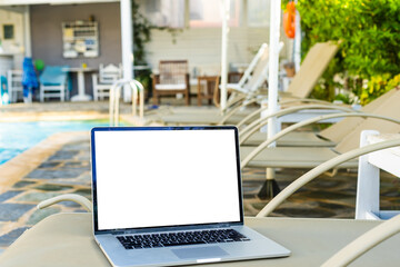 A laptop with an empty screen stands in the courtyard of a beautiful home garden, in Sunny weather.