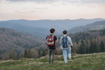 Back view on couple of travelers with walking sticks hiking high in mountains, Beauty of nature.