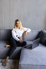 Obraz premium Calm woman working on a laptop, alone on a comfortable sofa in a cozy living room at home