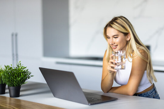 Shot of beautiful woman working with laptop while drinking glass of water on desk in office at home. Refreshment, hydration and Healthy habit concept.