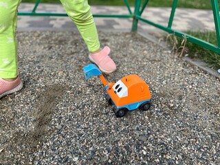 Games with toy excavator on the playground. A little child in green pants and pink shoes having summer activity with their toy lorry