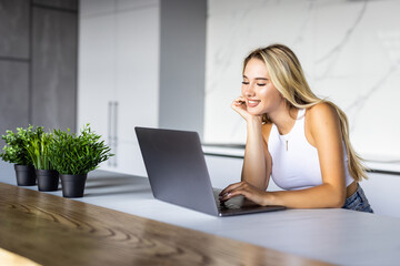 Happy young woman in the kitchen reading he news on her laptop