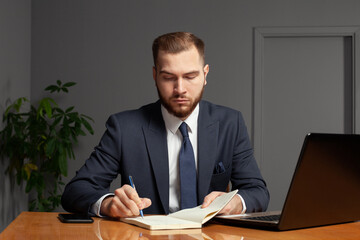 Handsome serious businessman is making notes while working on a laptop