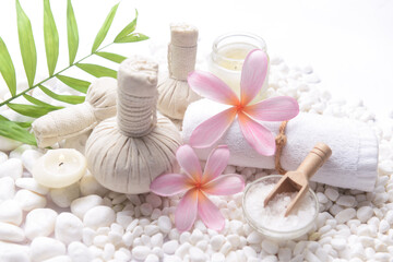 Spa setting with, herbal ,ball,  candle , rolled towel, salt in bowl ,green palm on pile white stones 

