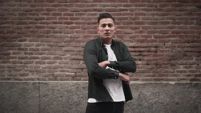 Hispanic young man gives a flirty and confident look at the camera while crossing his arms in slow motion