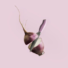 Flying radish cuttet with kitchen knife at purple background. Preparing healthy raw vegetable....