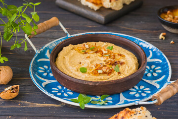 Appetizer or main course, eggplant dip with fried onions and walnuts in a brown clay plate on a metal tray on a brown wooden background. Rustic style.