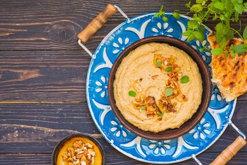 Appetizer or main course, eggplant dip with fried onions and walnuts in a brown clay plate on a metal tray on a brown wooden background. Rustic style.