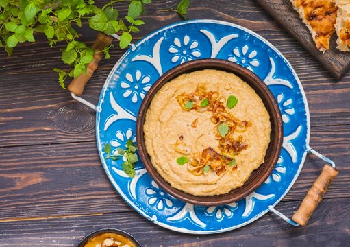 Appetizer or main course, eggplant dip with fried onions and walnuts in a brown clay plate on a metal tray on a brown wooden background. Rustic style.