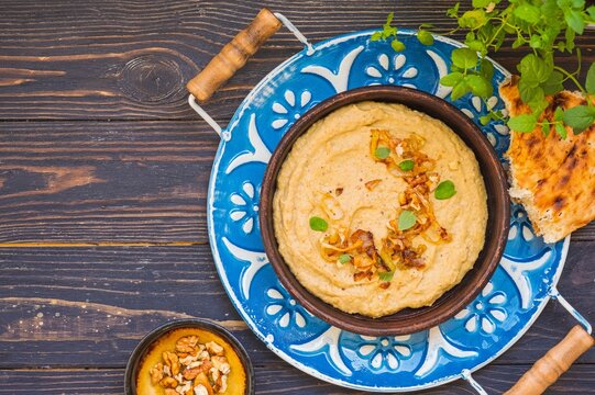 Appetizer or main course, eggplant dip with fried onions and walnuts in a brown clay plate on a metal tray on a brown wooden background. Rustic style.