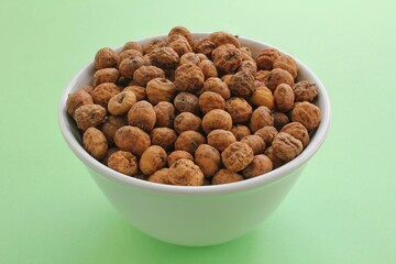 Chufa, tigernut, earth almond on ceramic bowl on green background. Healthy organic food concept. Tiger nut for flour, milk, traditional typical homemade cold fresh drink horchata from Valencia Spain