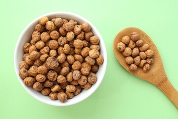 Chufa, tigernut, earth almond on white ceramic bowl and wooden spoon on green background. Healthy vegan food concept. Tiger nut for flour, oil, milk, traditional typical drink horchata Valencia Spain