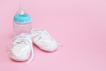 booties for a newborn and a bottle on a pink background copy space