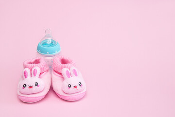 pink booties in the form of hares and a bottle on a pink background with copy space