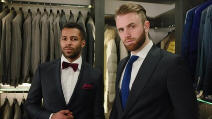 Concept of design clothing atelier in the luxury suit shop two charismatic and good looking men multiracial posing the suit in front of the camera