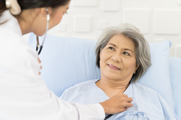 Fototapeta premium Nurse and elderly patient at hospital. Nurse using stethoscope examining elderly woman patient heartbeat. Nurse visiting and checking senior female patient. Health care concept