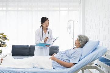Fototapeta premium Nurse, elderly patient and hospital. Nurse discussing and writing note to seek advice with elderly asian woman on bed at the hospital. People and health care concept