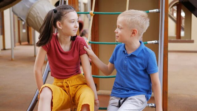 A boy and a girl are sitting on the playground talking and laughing.