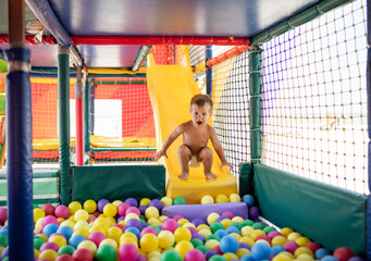 Obraz na płótnie Canvas The kid plays in the playroom and rolls down the slide into the pool with small balls