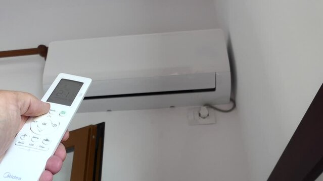 A man uses a remote control to adjust the air conditioning. 