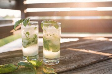 Refreshing drinks on wooden background in sunset light. Copy space. Summer lifestyle.