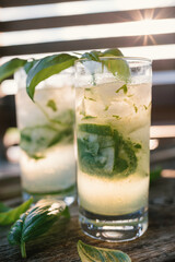 Cold refreshing glasses of clear liquid. Gin and tonic. Water garnished with basil and cucumber.