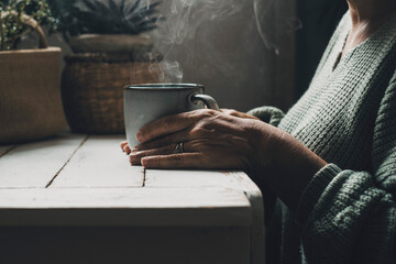 Close up of woman hands holding a hot cup of coffee or tea at home. People taking natural medicine...