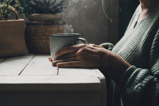 Close up of woman hands holding a hot cup of coffee or tea at home. People taking natural medicine for health lifestyle. Concept of healthy herbal tea drinking. Aged female with mug indoor closeup