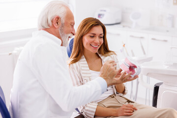 Dentist explaining medical procedure to patient on plastic jaw model