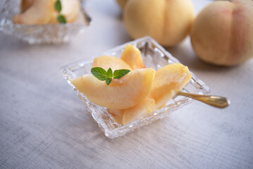 Pieces of japanese white peach in glass bowl on wooden background.