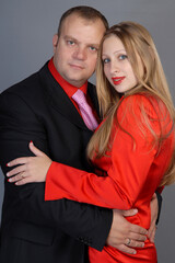 portrait of a man in a black business suit hugging a beautiful fair-haired girl in a red suit. loving couple