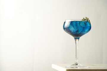 Dark blue drink in a vintage glass for sparkling wine - pea flower tea or blue curacao sirup cocktail with thyme branches on white backgroud. Copy space for text