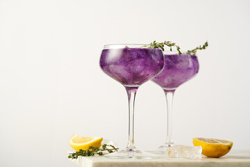 a purple drink in a vintage glass for sparkling wine - pea flower tea or blue curacao sirup cocktail with thyme branches on white background. Copy space for text