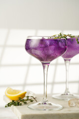 a purple drink in a vintage glass for sparkling wine - pea flower tea or blue curacao sirup cocktail with thyme branches on white background. Copy space for text