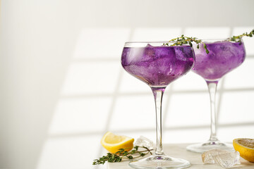 a purple drink in a vintage glass for sparkling wine - pea flower tea or blue curacao sirup cocktail with thyme branches on white background. Copy space for text