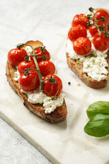 A sandwich with roasted cherry tomatoes with branch, fresh cottage cheese, green basil on a slice of whole wheat bread on a marble board on grey background
