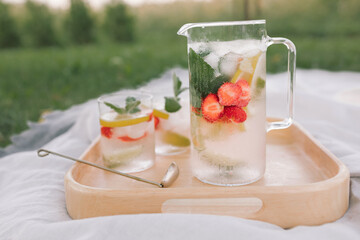 Summer non-alcoholic drinks with berries and mint on wooden tray in nature. Summer picnic in the countryside.