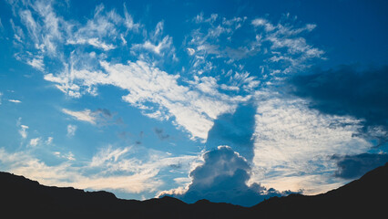 Dramatic white clouds on the blue sky in evening. Silhouette of mountains.   