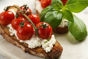 Fototapeta na wymiar A sandwich with roasted cherry tomatoes with branch, fresh cottage cheese, green basil on a slice of whole wheat bread on a marble board on grey background
