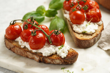 A sandwich with roasted cherry tomatoes with branch, fresh cottage cheese, green basil on a slice of whole wheat bread on a marble tray on grey background